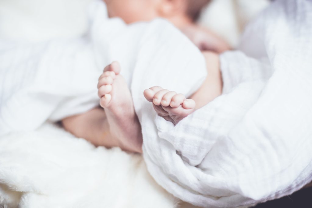 Closeup of a newborn baby's feet nestled around a white blanket.